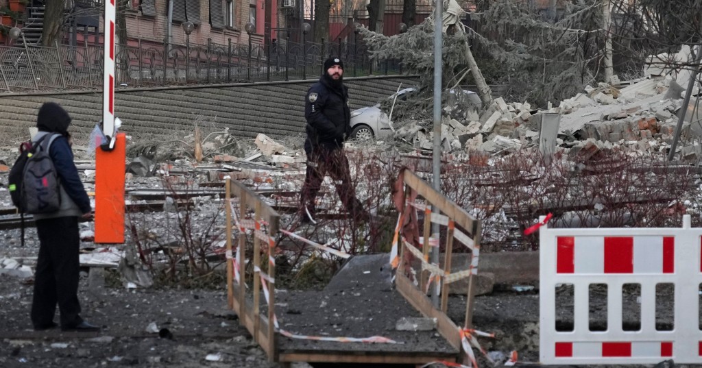 People stand next to damaged building at the scene of Russian shelling in Kyiv, Ukraine, Saturday, Dec. 31, 2022. (AP Photo/Efrem Lukatsky)