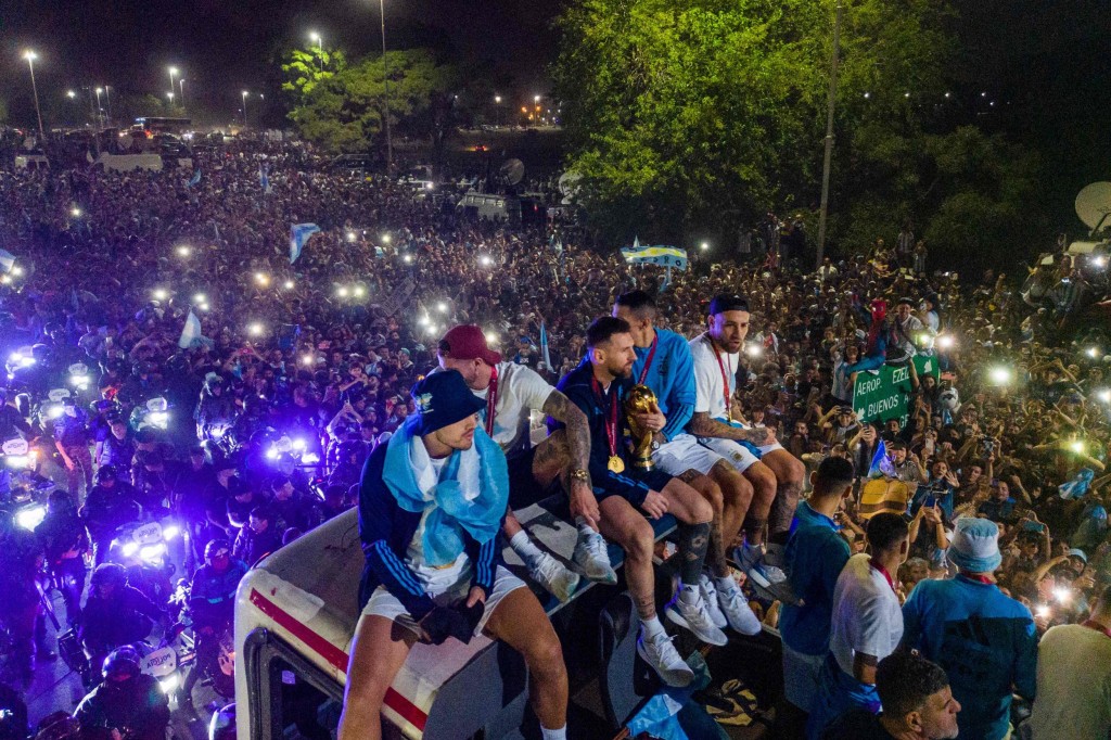 Argentina's captain and forward Lionel Messi (C) holds the FIFA World Cup Trophy on board a bus as he celebrates alongside teammates and supporters after winning the Qatar 2022 World Cup tournament in Ezeiza, Buenos Aires.