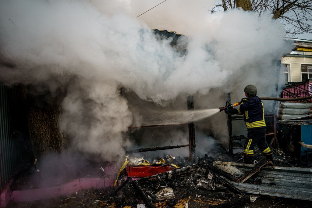 TOPSHOT - A rescuer extinguishes a fire in a burning shop after Russian shelling to Ukrainian city of Kherson on December 24, 2022, where five were killed and 20 injured. - Ukrainian President Volodymyr Zelensky on December 24, 2022 blasted Russian