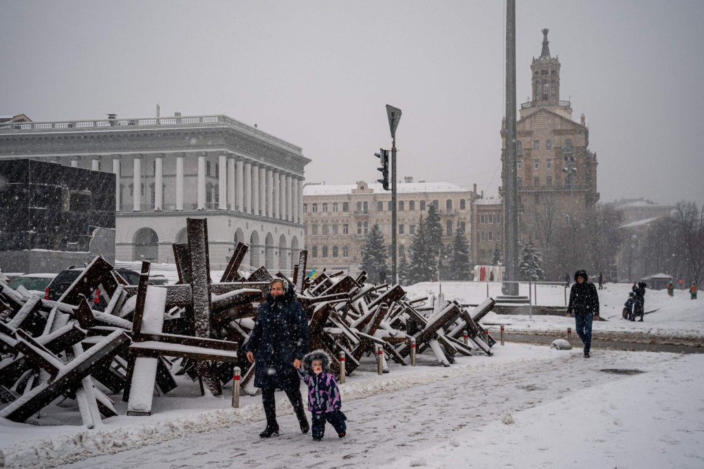 TOPSHOT - A woman and child walk past anti-tank steel hedgehogs covered with snow along Independence Square in the Ukrainian capital Kyiv on December 15, 2022, amid the Russian invasion of Ukraine. (Photo by Dimitar DILKOFF / AFP) (Photo by DIMITAR DILKOFF/AFP via Getty Images)