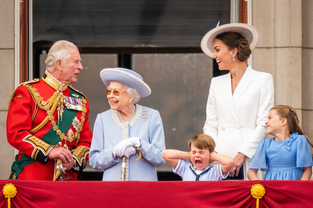 From left to right: King Charles, The Queen, Prince Louis (who is holding his. hands over his ears and pulling a screaming face) Kate Middleton and Princess Charlotte