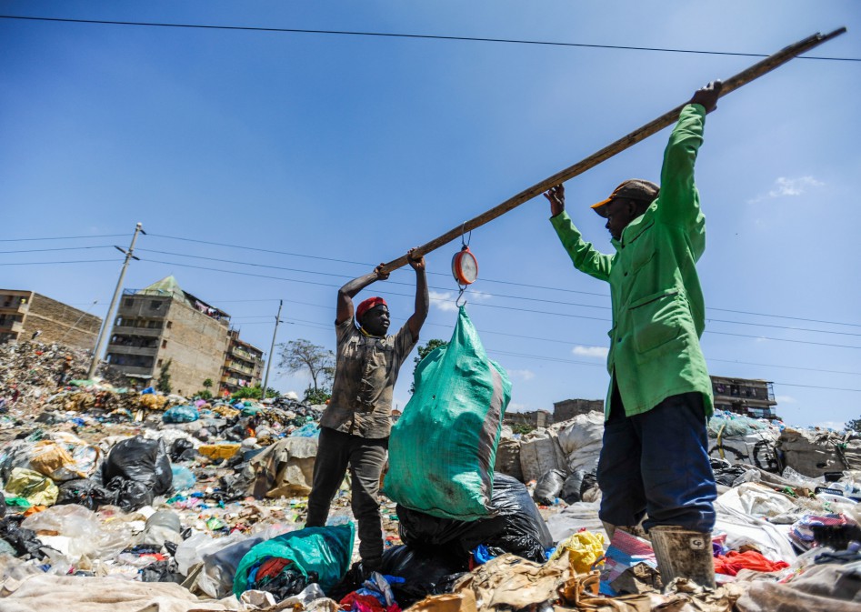 Two men hold a stick that helps weigh the rubbish. A kilo of plastic is worth 11p.