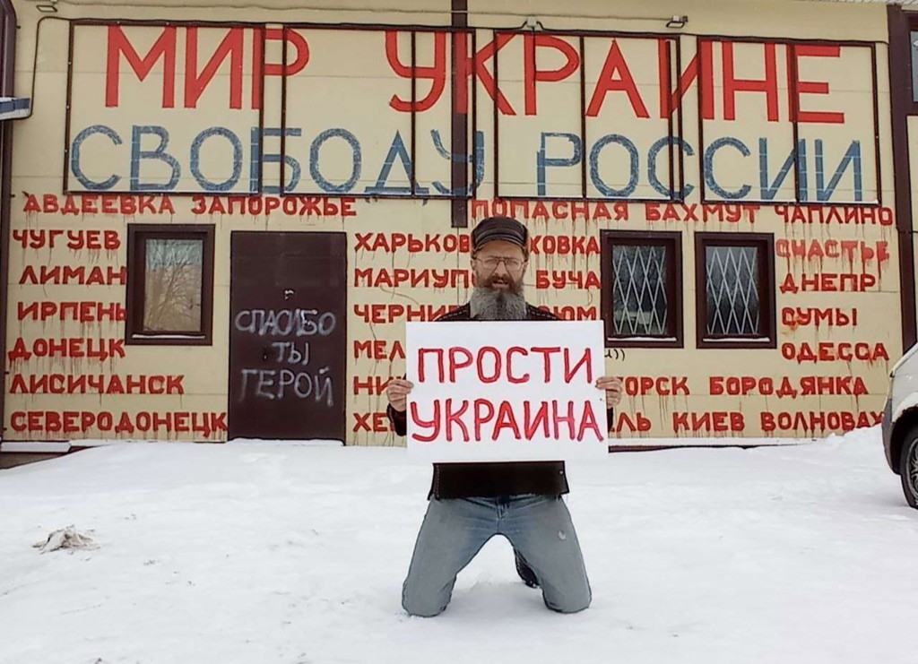 Grocery shop owner Dmitry Skurikhin holds a poster 'Forgive us, Ukraine' in front of his shop. The writing on the top of the wall reads: 'Peace to Ukraine, freedom to Russia'.