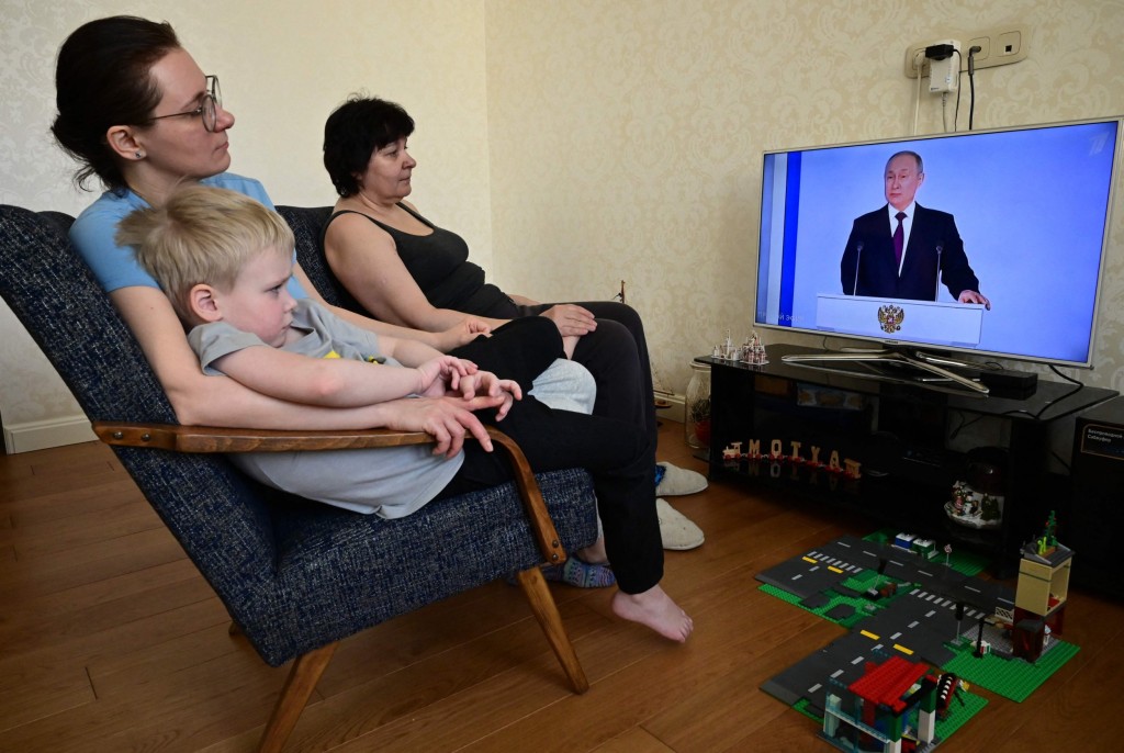 A family watches a TV broadcast of Russian President Vladimir Putin's annual state of the nation address in Moscow on February 21, 2023. (Photo by Yuri KADOBNOV / AFP) (Photo by YURI KADOBNOV/AFP via Getty Images)