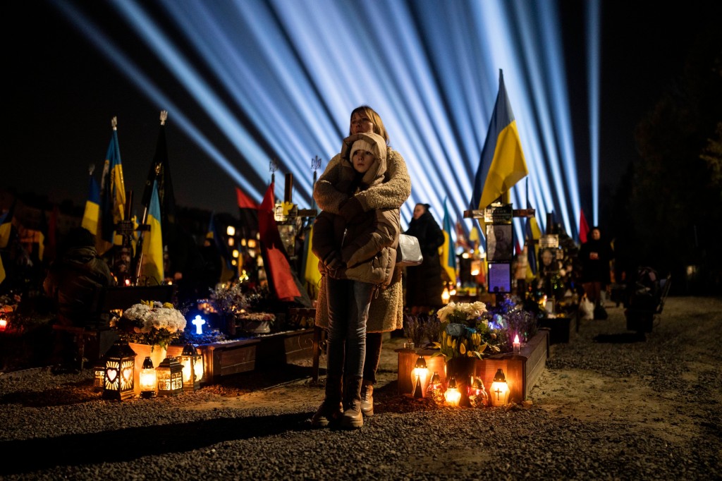 A woman holds her daughter as they listen to a prayer for fallen soldiers at the cemetery.